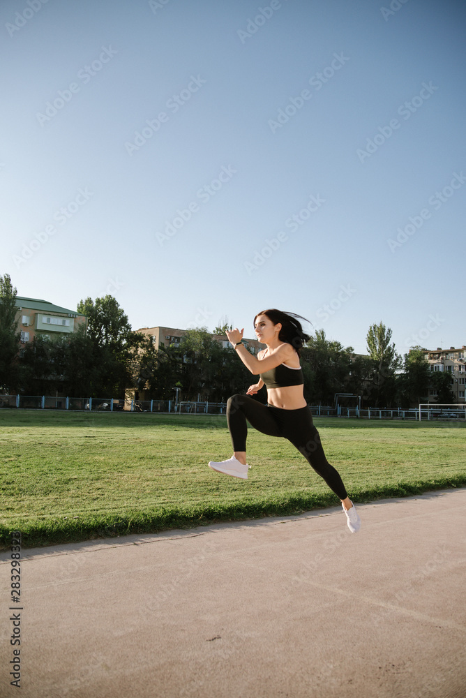 Young woman running during sunny morning on stadium track