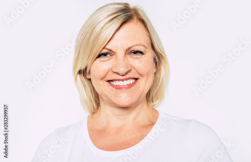 Close up portrait of happy smiling and beautiful blonde senior woman isolated in studio and posing with smile on camera