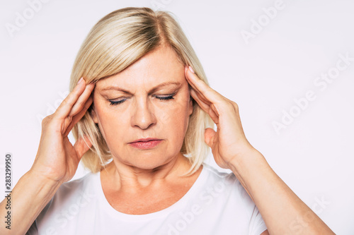 Portrait of beautiful blonde senior woman with severe headache while she holds hands on her head with closed eyes.