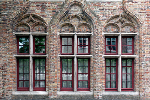 Old brick wall whith three windows with red frames