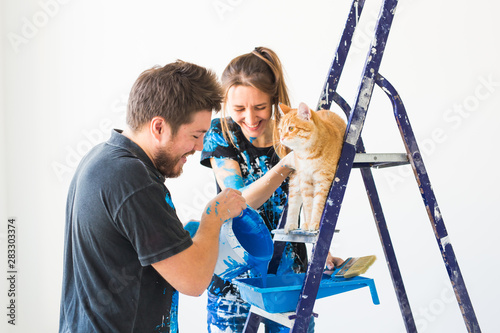 People, renovation and repair concept - portrait of happy couple with cat pour paint