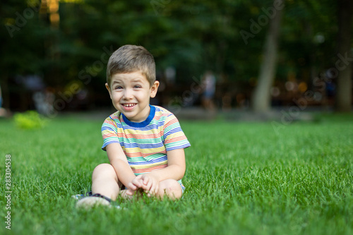baby boy sitting on green grass outdoor playing.Child lying on grass © Delete