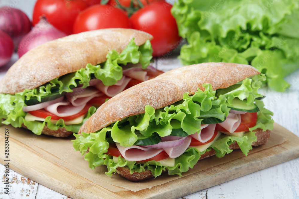 Two sandwiches with fresh vegetables, ham and cheese in ciabatta bread Two sandwiches with fresh vegetables, ham and cheese in ciabatta bread