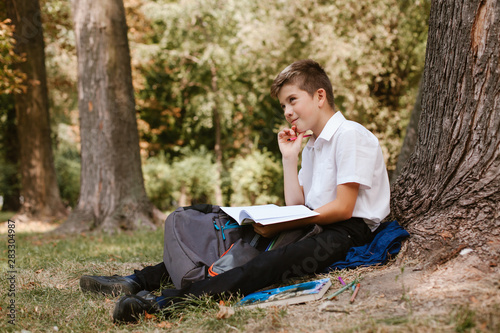 Schoolboy in a park under a tree doing homework.schoolboy sitting under a tree in the park