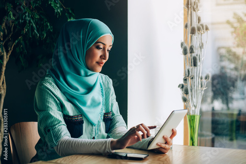 Beautiful young arabic girl in hijab posing for camera at cafe.