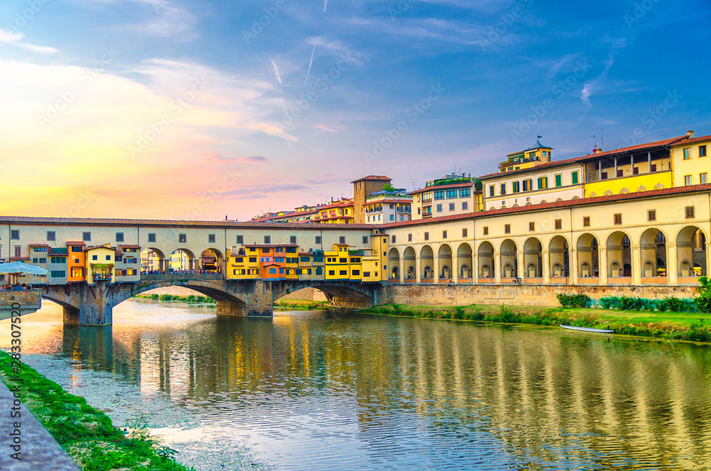 Ponte Vecchio bridge with colourful buildings houses over Arno River reflecting water and embankment promenade archways, historical centre of Florence city, blue evening sky clouds, Tuscany, Italy