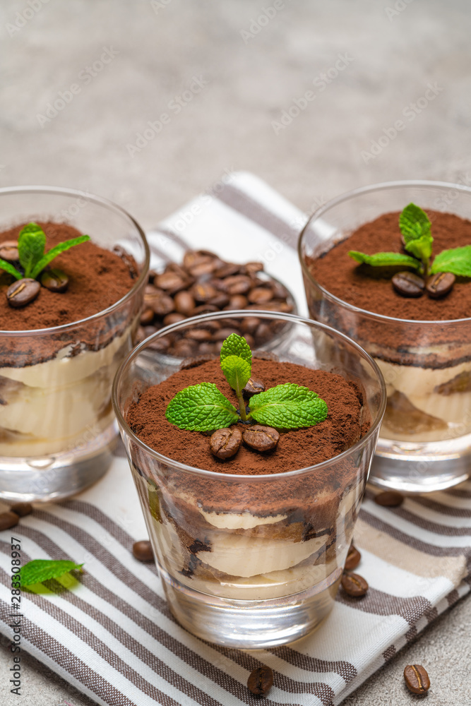Classic tiramisu dessert in a glass on kitchen towel on concrete background Classic tiramisu dessert in a glass on kitchen towel on concrete background