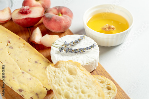Fototapeta Naklejka Na Ścianę i Meble -  Top view different types of cheeses on wooden cutting board. Cheese with fig peach, honey, ciabatta and nuts, glass of red wine. Stylish food flat lay on grey background. Copy space. Soft focus