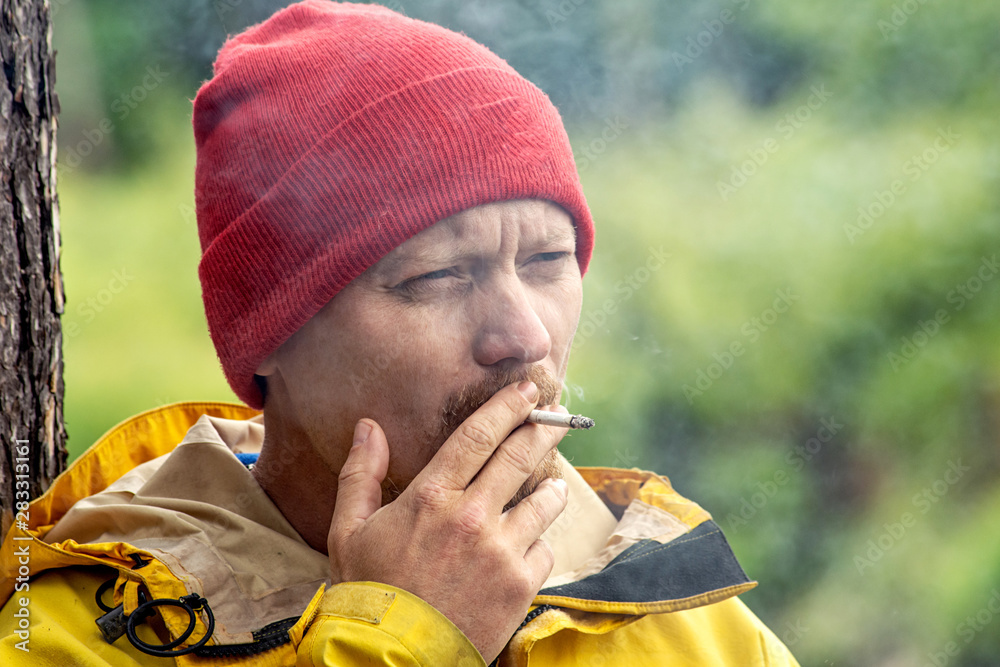 Εκτύπωση καμβά brutal man smoking a cigarette in green forest, outdoor hipster portrait
