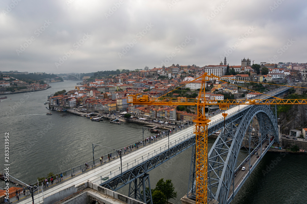 View to the old city of Porto with the D. Luis bridge and construction crane. Cloudy sky.