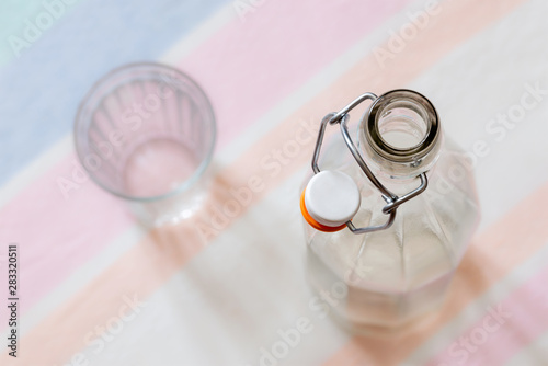 Top view of a glass bottle with a wire bail clasp ceramic stopper, and a drink glass, on a blue, pink and orange stripped tablecloth