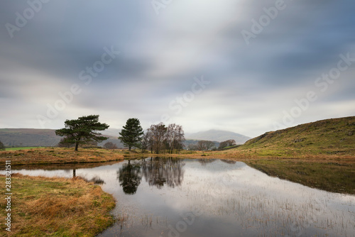 Stunning landscape image of dramatic storm clouds over Kelly Hall Tarn in Lake District during late Autumn Fall afternoon