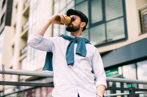 Enjoying fresh coffee. Handsome young man in casual wear holding disposable cup and smiling while walking through the city street