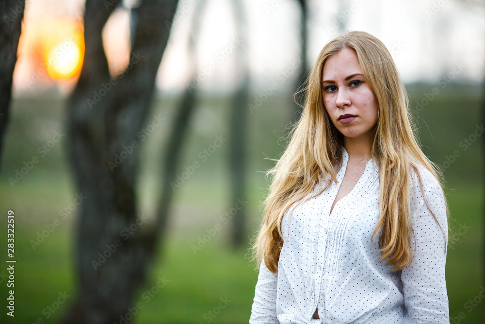 Portrait of a young cute caucasian girl with problem skin in white shirt on the street in the park at sunset in autumn.