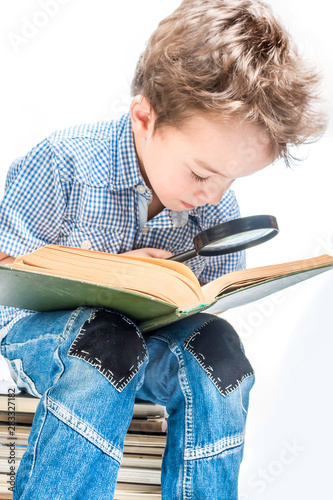 Cute boy with a magnifying glass is reading a book on a white background. Close-up.