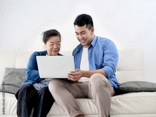 Asian man teaching his mother using laptop at home, technology concept.