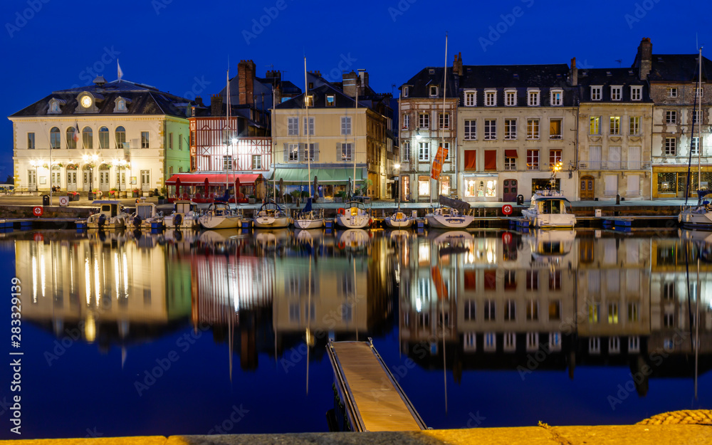 View of the picturesque harbour of Honfleur, yachts and old houses reflected in water. Blue hours. France, Normandy, Europe.