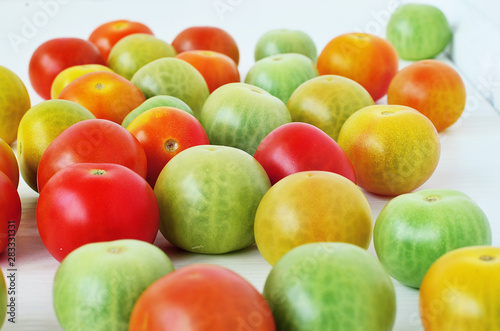 Red  green and yellow tomatoes on white background. Tomatoes of different colors and varieties. Juicy tomatoes on a white table. Colorful vegetables.