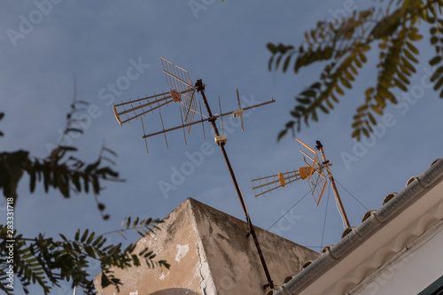 two television antennas on a rooftop in front of blue sky photo