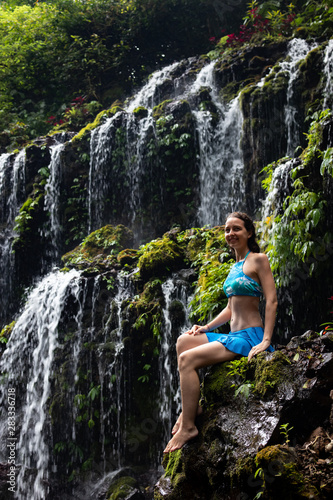Travel lifestyle. Young traveler woman sitting at waterfall in tropical forest. Banyu Wana Amertha waterfall Wanagiri, Bali, Indonesia.