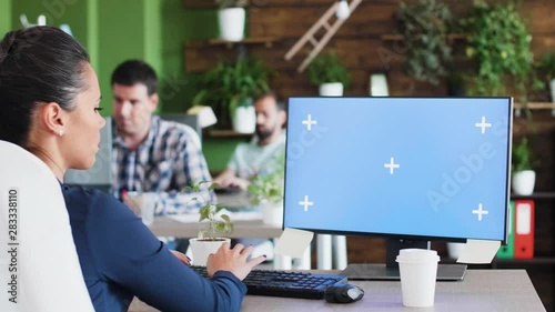 Young business woman working on her computer. Empty mock-up screen. Coworkers in the backgroound.