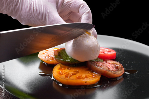 Buratta mozzarella with pesto sauce and tomatoes on a black plate photo