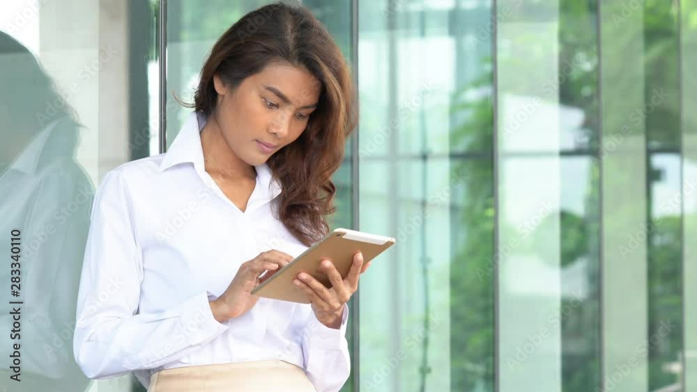 4K Young adult asian businesswoman standing out of office building using digital tablet with internet wireless technology for online stocks trading business. Freelance working business outdoor concept 4K Young adult asian businesswoman standing out of office building using digital tablet with internet wireless technology for online stocks trading business. Freelance working business outdoor concept