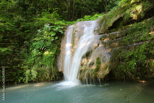 Blue waterfall in green trees. puddle. sun and nature.