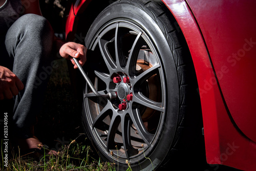 man hand with wrench tightens a beautiful car wheel towards a red car