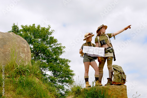 Two young girls dress up as explorers.They pose in  a rocky outdoor area dressed with jungle hats and khaki safari clothes.