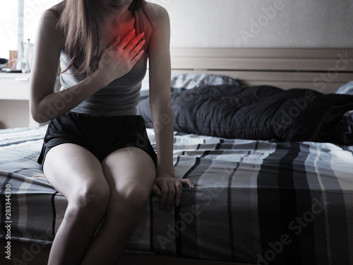 Asian female clutching her chest, acute pain possible heart attack .