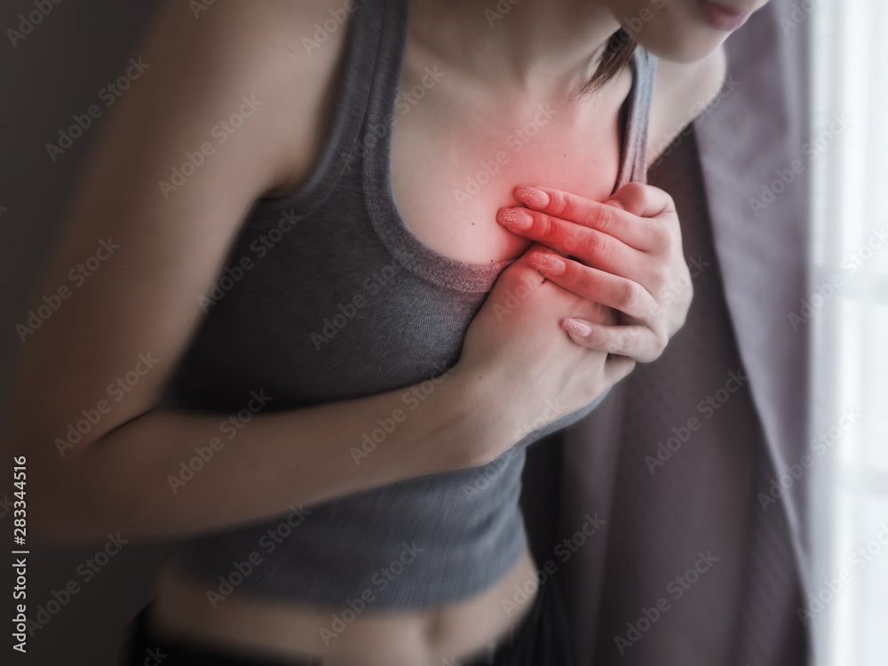 Asian female clutching her chest, acute pain possible heart attack .