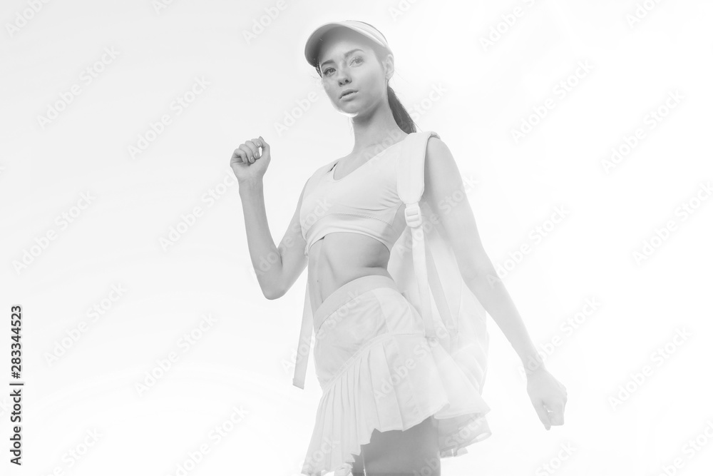Fototapeta premium Sports woman posing in fashion sportswear on sunny sky background. Beautiful slim girl in trendy skirt, top, cap and backpack. Black and white.