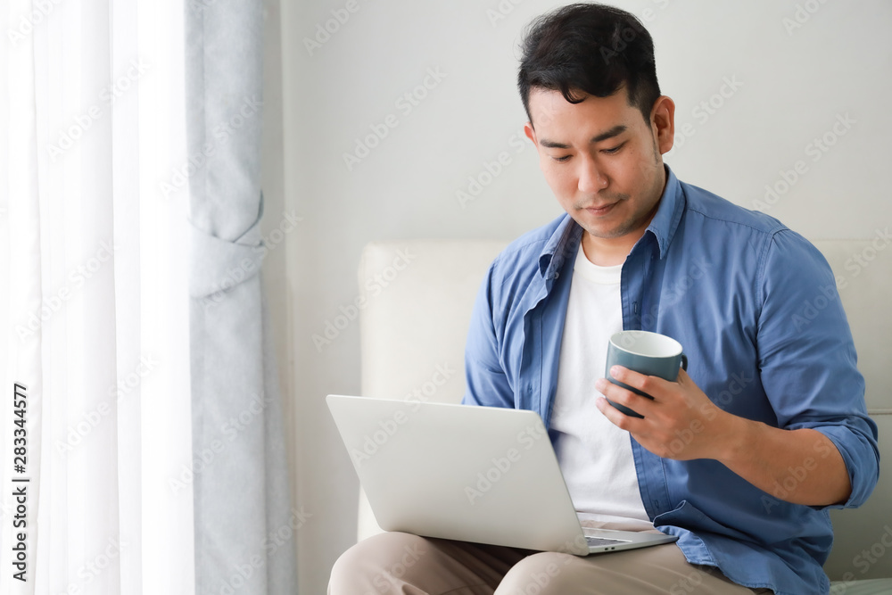 Asian handsome man working with laptop computer and drink coffee in living room happy and smile face Asian handsome man working with laptop computer and drink coffee in living room happy and smile face