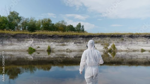 Man in a protective suit and respirator takes tests from a polluted river or lake, rises and go back, then observes the chemical reaction of water in a test tube. A scientist takes samples in vitro 4K