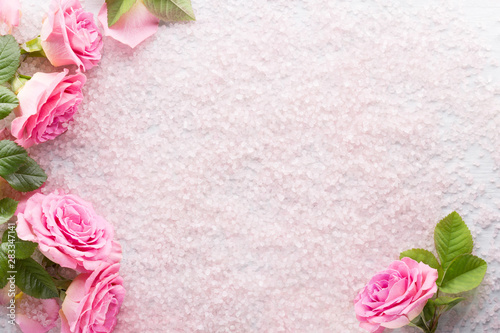 Spa salt crystals and pink roses with green leaves. Flat lay.