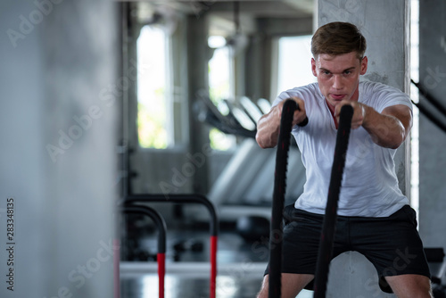 Young adult caucasian athlete sport bodybuilding man in sportswear doing cardio battle rope exercise workout fitness pumping up muscles during training class in gym sport club for strong healthy.