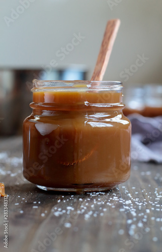 Open jar of salted caramel sauce over a rustic table. Selective focus with blurred background.