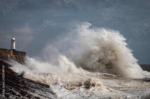Huge breaking waves next to a lighthouse on a stormy day (Porthcawl, Wales, UK) photo