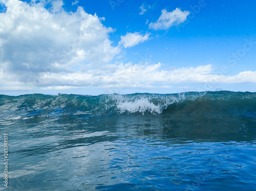 Waves on the ocean with a bright blue fluffy clouded day.