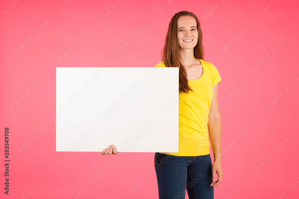 Young woman in yellow t shirt holds blank banner for advertisment over vibrant pink background Young woman in yellow t shirt holds blank banner for advertisment over vibrant pink background