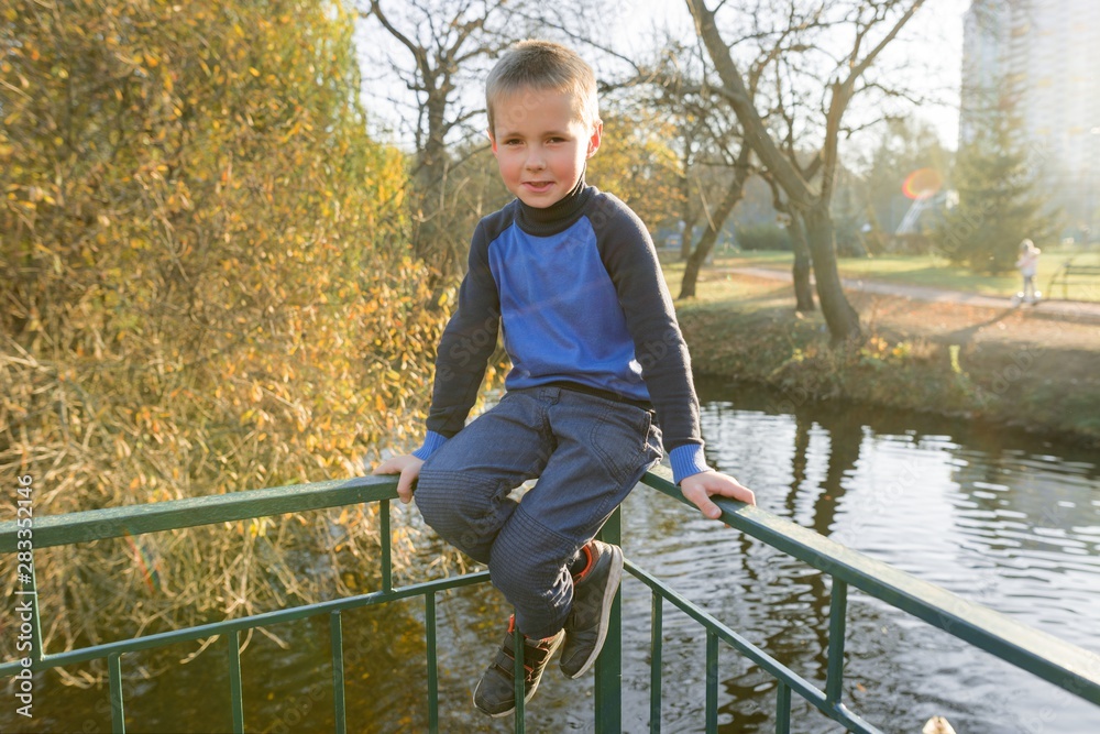 Portrait of boy child on bridge in sunny autumn park, background pond leaf fall Portrait of boy child on bridge in sunny autumn park, background pond leaf fall