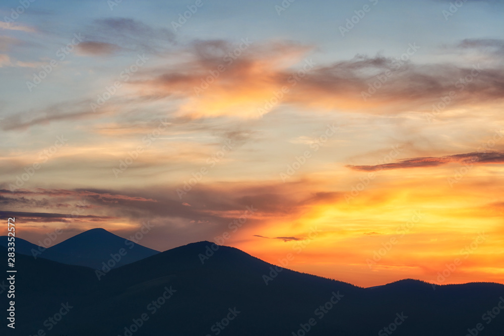 Background of bright orange sky at sunset. Mountain silhouettes.