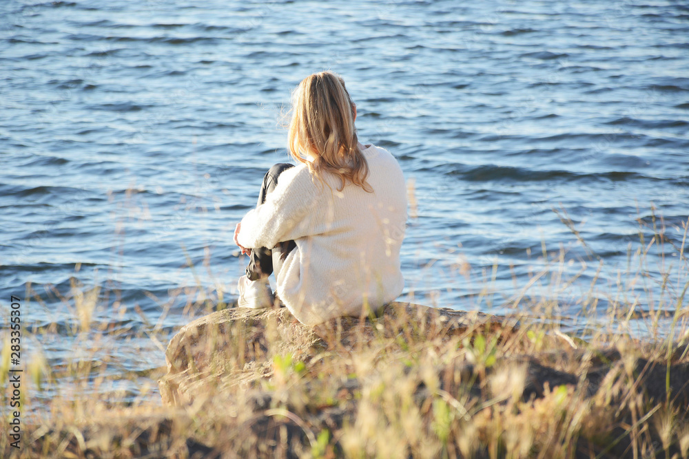 Young woman sitting on a rock peacefully gazing at the lake thinking about life