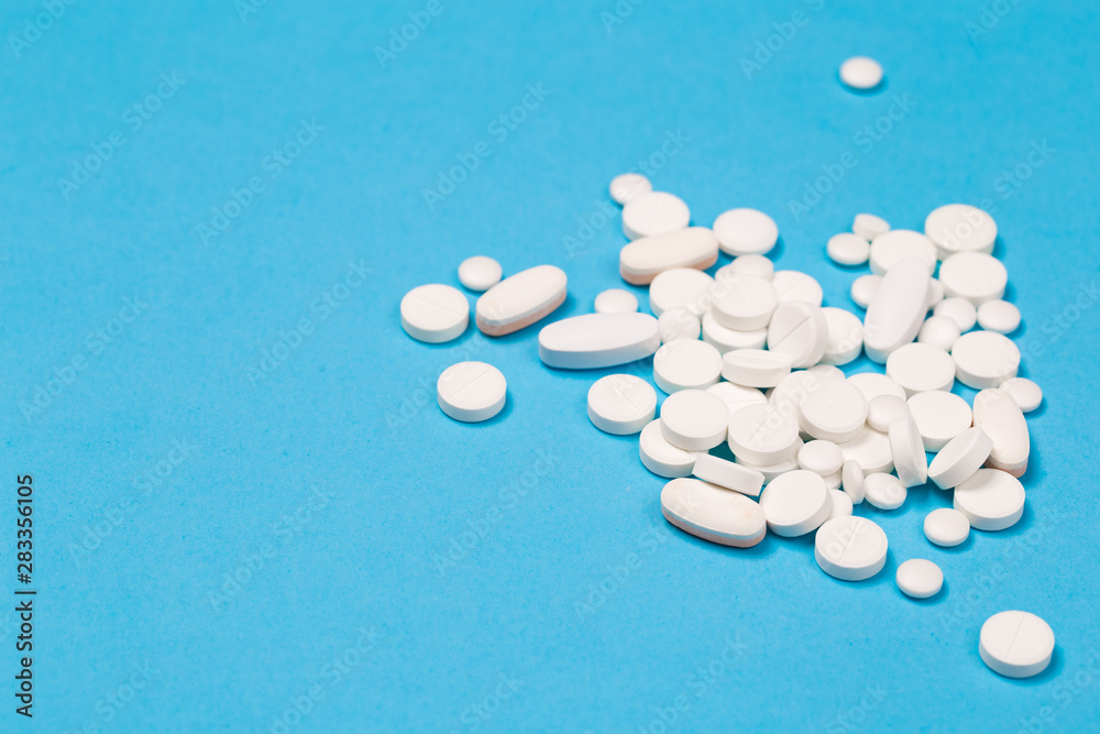 White Pills are scattered over a blue background. Close up. Medical background.