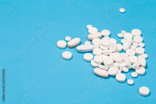 White Pills are scattered over a blue background. Close up. Medical background.