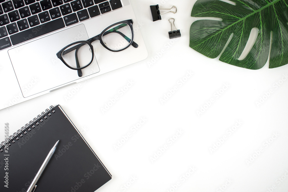 Flat lay, top view office table desk. Workspace has a laptop, notebook, pen, clip board, eye glasses and leaves with a copy area. Flat lay, top view office table desk. Workspace has a laptop, notebook, pen, clip board, eye glasses and leaves with a copy area.
