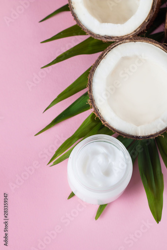 Ripe half cut coconut with cream and green leaves on a pink background.
