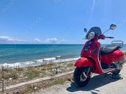 Red scooter parked by the Aegean Sea on holiday in Greece