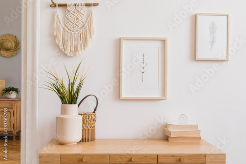 Stylish and modern boho interior of living room with mock up photo frames, flowers in vase, wooden desk, beige macrame and elegant accessories. Design home decor. Bohemian concept. Mockup ready to use